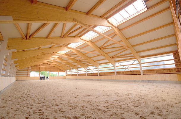 Innenraum einer hellen Reithalle mit Holzbinder-Konstruktion