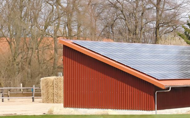 Landwirtschaftliche Halle mit roter Trapezblechfassade und großflächiger Photovoltaikanlage auf dem Satteldach.