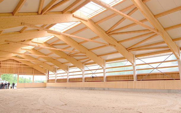 Innenraum einer hellen Reithalle mit Holzbinder-Konstruktion