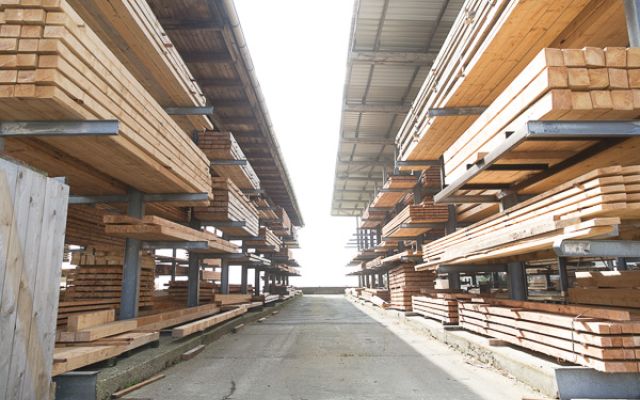 Gestapelte Holzbretter und Balken in einem überdachten Holzlager mit Mittelgang